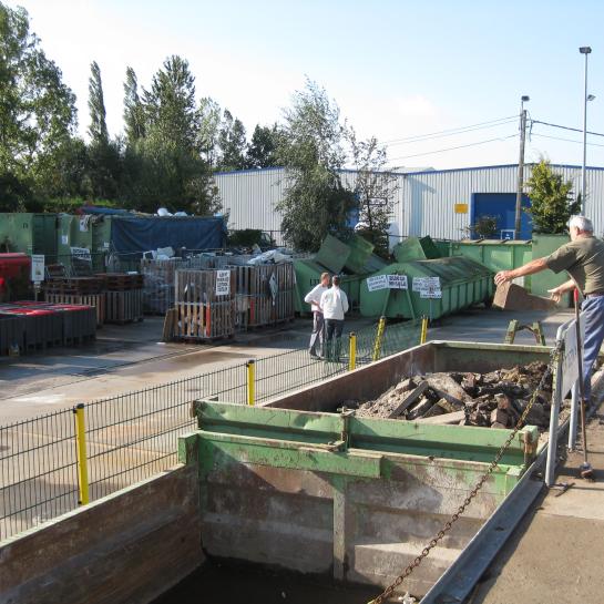 Een bezoeker deponeert afval in een container op het recyclagepark